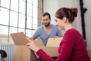 Attractive young couple moving house getting ready to unpack a cardboard carton of personal possessions below a big window.jpeg