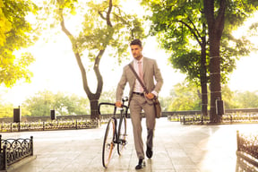 Confident young businessman walking with bicycle on the street in town .jpeg