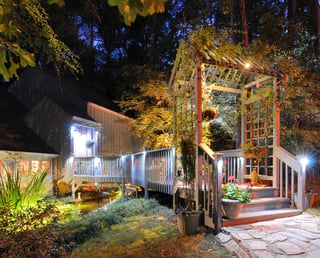 House exterior with porch walkway over a pond and lighting in the woods.jpeg